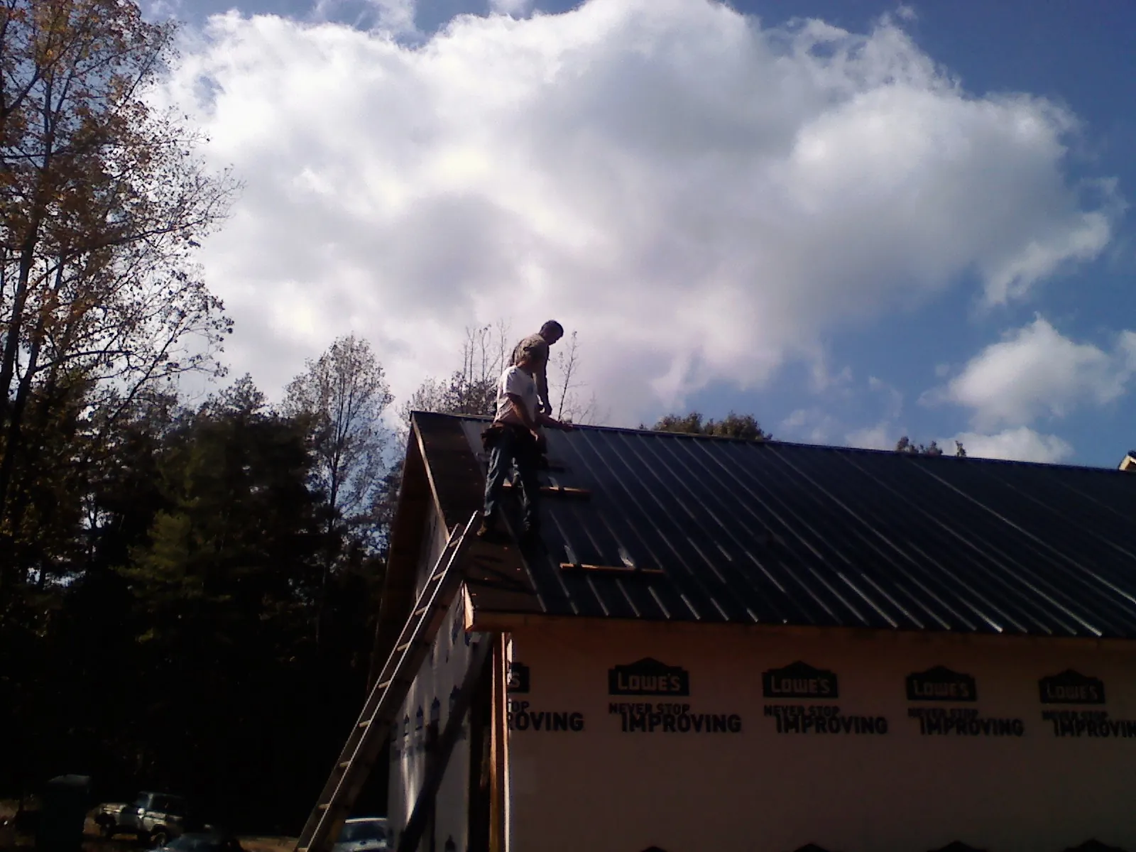 Roofer fastening dark metal panels high against a cloudy sky, from a Roof Inspection job in Maple City
