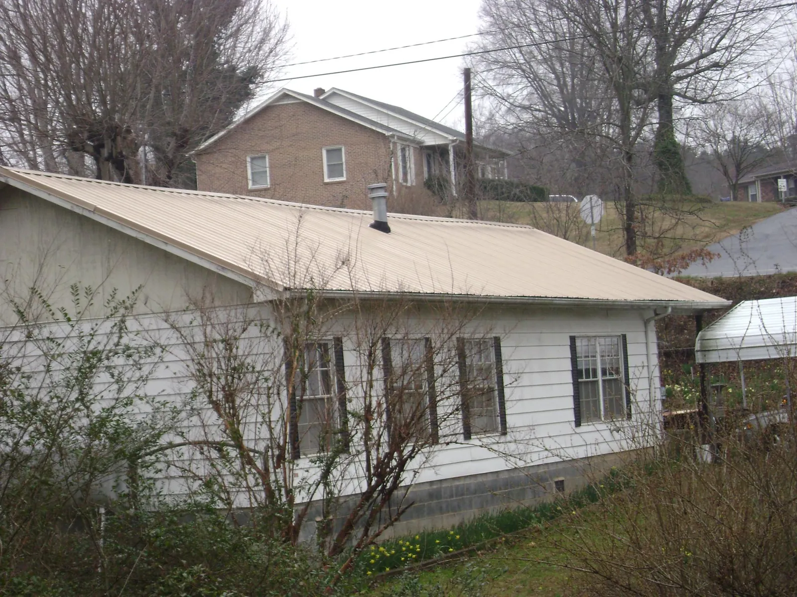 Tan metal roof on a white sided house set into a hillside — Commercial Roofing by Roofing Brothers in Maple City
