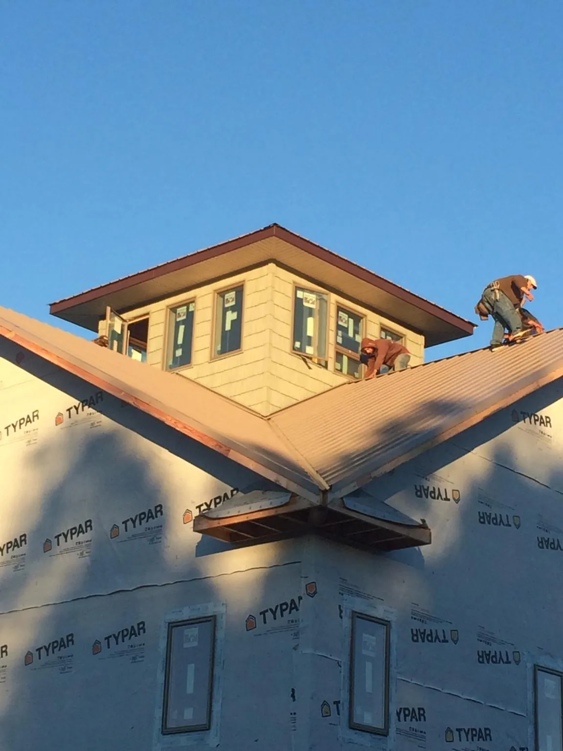 Roofers working around a rooftop cupola on a new metal roof at sunset — Roof Waterproofing in Maple City by Roofing Brothers
